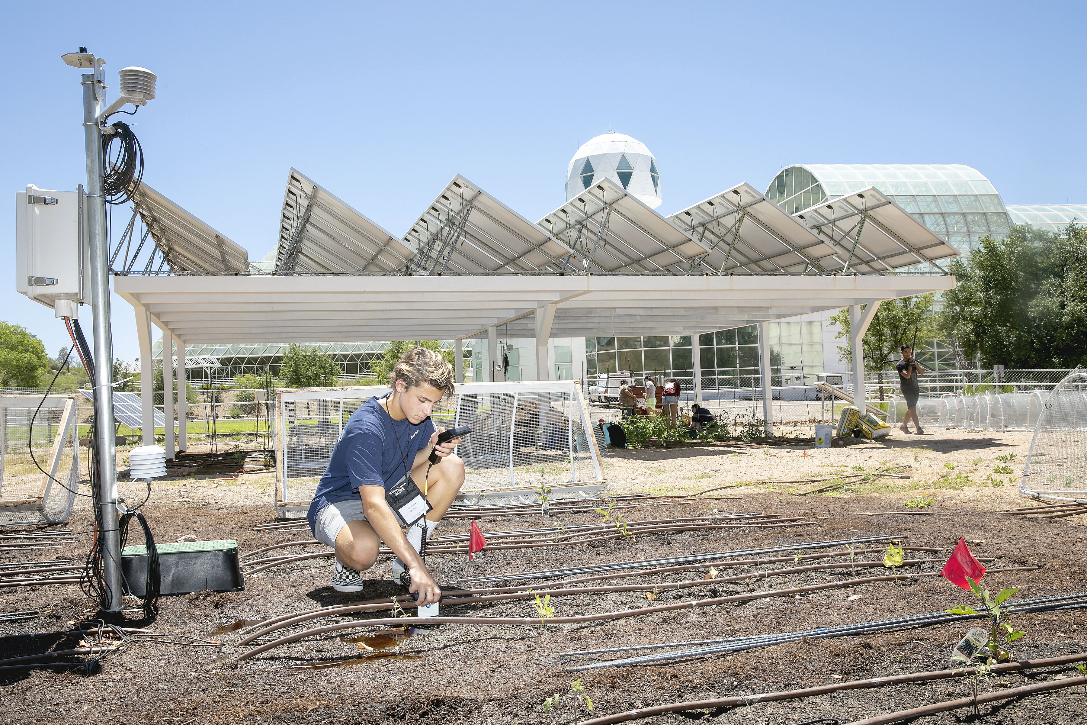 Student in dirt field conducting research in front of Biosphere 2